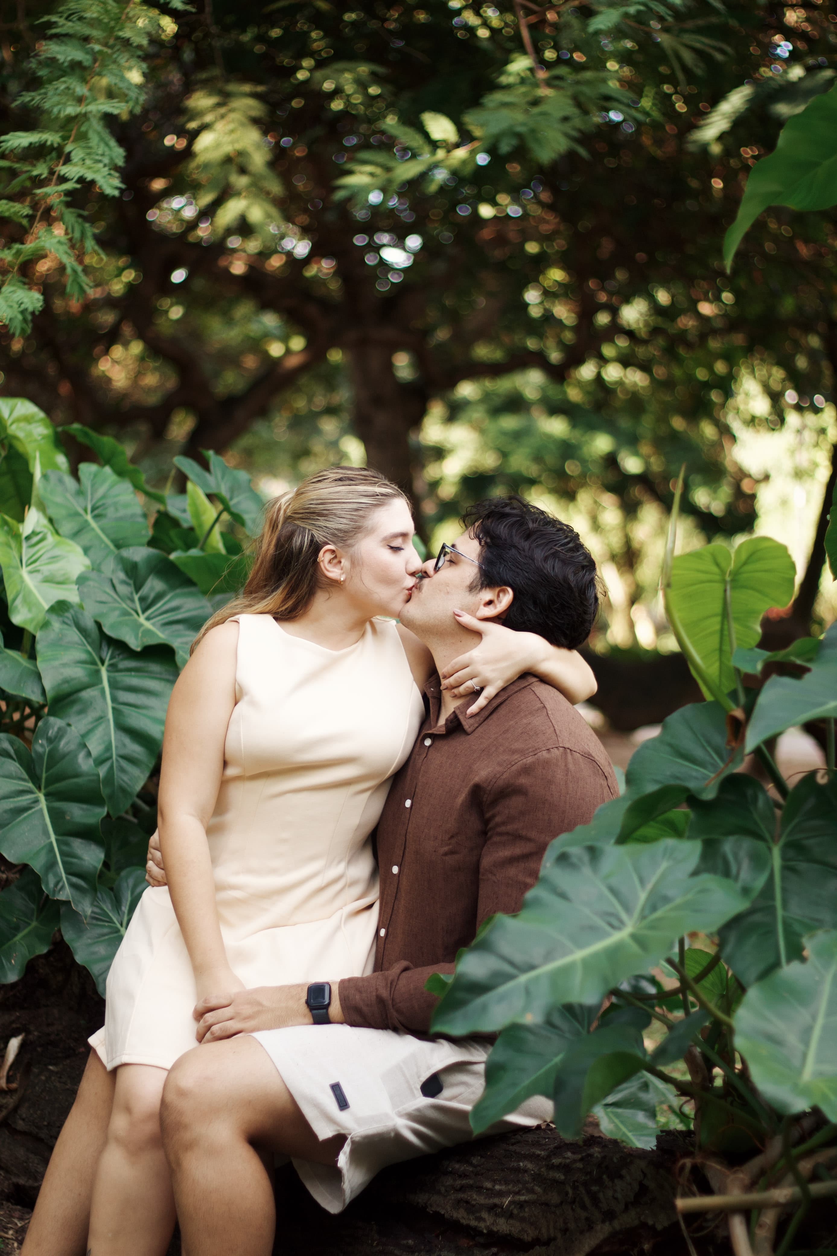 Gabrielle e Pedro se beijam sentados em meio à folhagem tropical